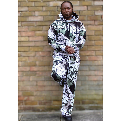 Person wearing GeoLux Unisex Hoodie with bold digital print, paired with matching trousers, standing against a brick wall.