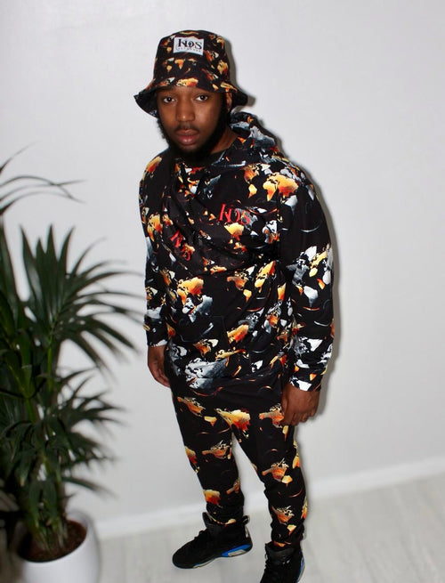 Man wearing Ember Blaze Men’s Hoodie with vibrant print and matching bucket hat, standing in a modern setting.