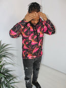 Man wearing a Crimson Peacock Mosaic hoodie with vibrant pink and red geometric print against a white background.