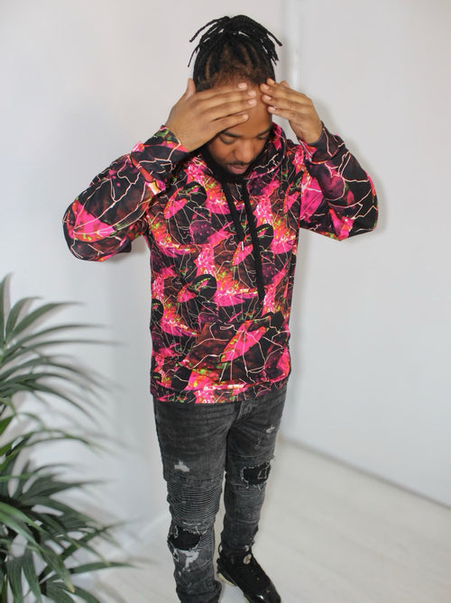 Man wearing a Crimson Peacock Mosaic hoodie with vibrant pink and red geometric print against a white background.