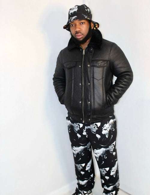 Man wearing a black leather jacket and abstract print joggers, showcasing urban streetwear style.